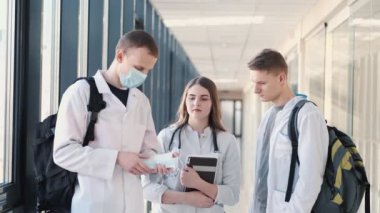 Kitapları ve çantaları olan tıp öğrencileri modern bir salonda bir şey tartışıyorlar.