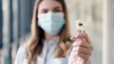 Tek kullanımlık maskeli bir kadın, test tüpünde papatya tutuyor.