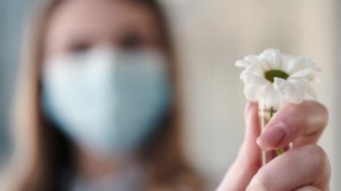 Tek kullanımlık maskeli bir kadın, test tüpünde papatya tutuyor.