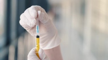 Tıbbi eldivenli hemşire sarı solüsyonlu şırıngayı test ediyor.