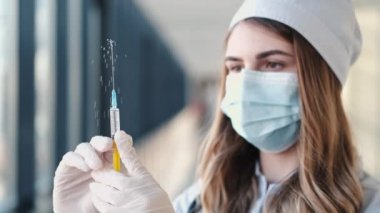 Tıbbi eldivenli hemşire ve tek kullanımlık maske sarı solüsyonlu şırıngayı test ediyor.