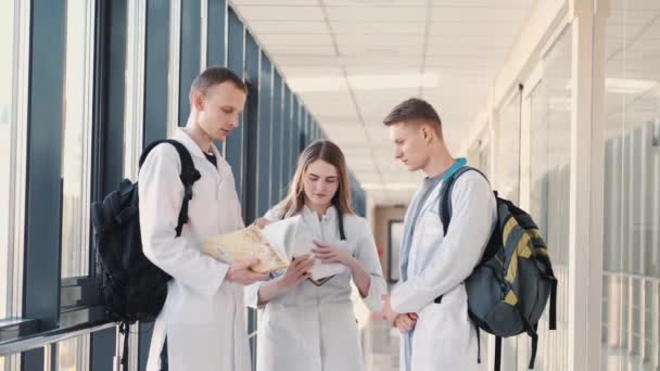 Medicinska studenter med böcker och väskor diskuterar något i en modern hall — Stockvideo