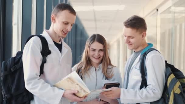 Studenti medicíny s knihami a taškami diskutují o něčem v moderním sále — Stock video