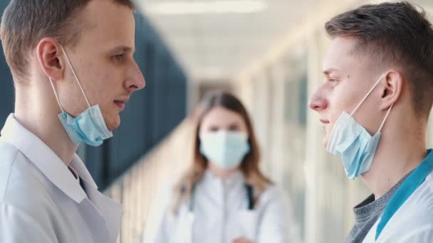 Zwei Männer in Atemschutzmasken stehen sich gegenüber, eine Frau daneben — Stockvideo