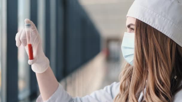 Woman doctor in a medical hat and a mask is holding a vial with blood — Stock Video
