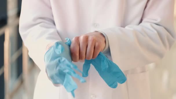 Доктор в халате надевает медицинские голубые перчатки — стоковое видео