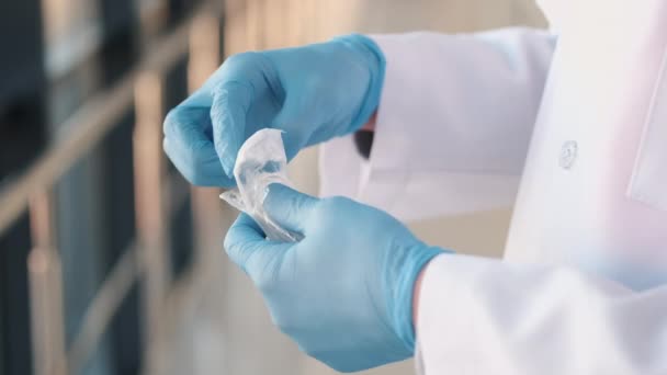 El médico con una bata y guantes médicos está desempacando una jeringa nueva — Vídeo de stock