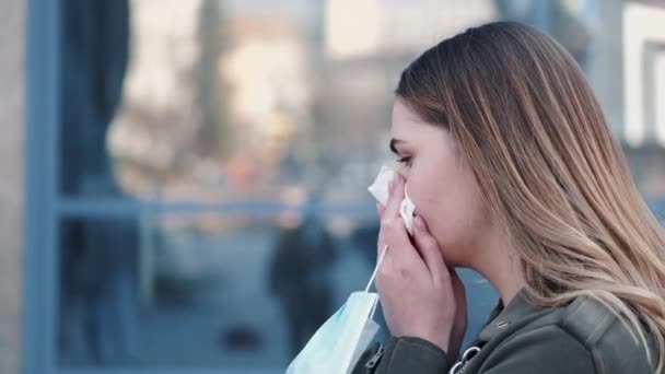 Mladá žena stojící venku kýchá a nosí masku na jedno použití — Stock video