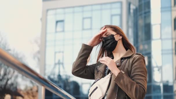 Seorang wanita muda dengan smartphone dekat scyscraper mengenakan respirator hitam — Stok Video