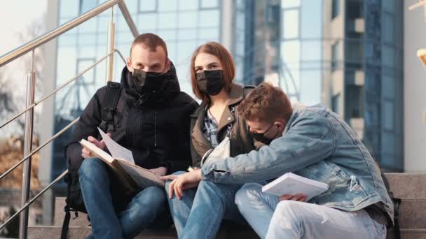 Los jóvenes están sentados en las escaleras fuera de un edificio con máscaras negras . — Vídeos de Stock