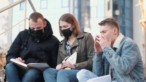 Unga människor sitter på trappor utanför en bulding bär svarta masker. — Stockvideo