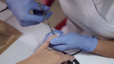 Güzellik uzmanının ellerine yakın çekim. Tırnakları makasla temizliyor.