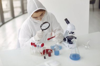 Giyim kuşamındaki bilim adamı bir laboratuarda koronavirüs örneğini inceliyor.