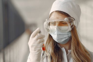 Maskeli ve üniformalı bir kadın elinde bir tüp tutuyor.