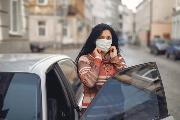 Mujer en una máscara está en la calle junto al coche —  Fotos de Stock
