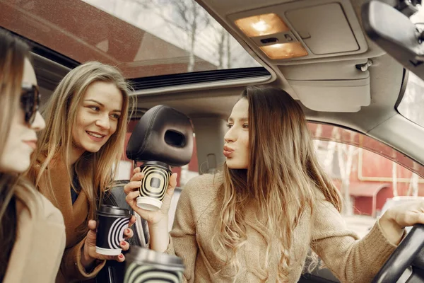 Three girls sitting inside the car and drinking a coffee