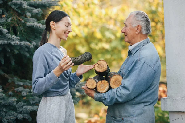 Abuelo con nieta en un patio con leña en las manos — Foto de Stock