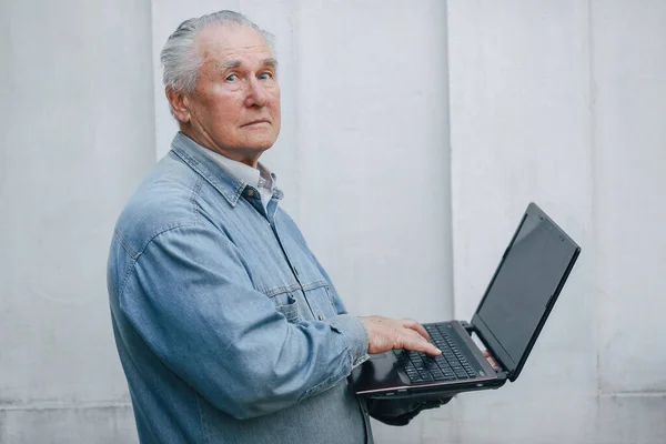 优雅的老人站在灰蒙蒙的背景上，用笔记本电脑 — 图库照片