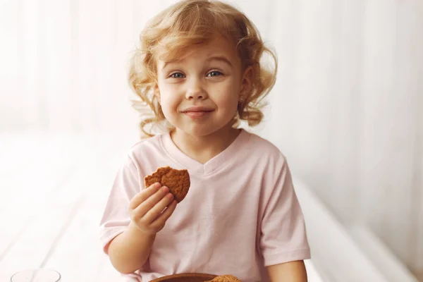 Menina bonito sentado em um estúdio e comer biscoitos — Fotografia de Stock