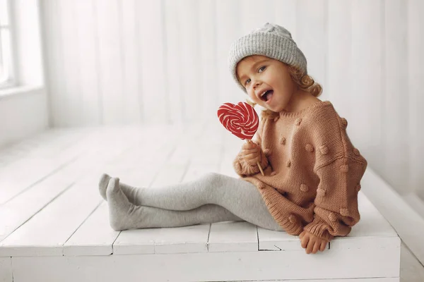 Χαριτωμένο κοριτσάκι που κάθεται σε ένα στούντιο και τρώει γλυκά. — Φωτογραφία Αρχείου