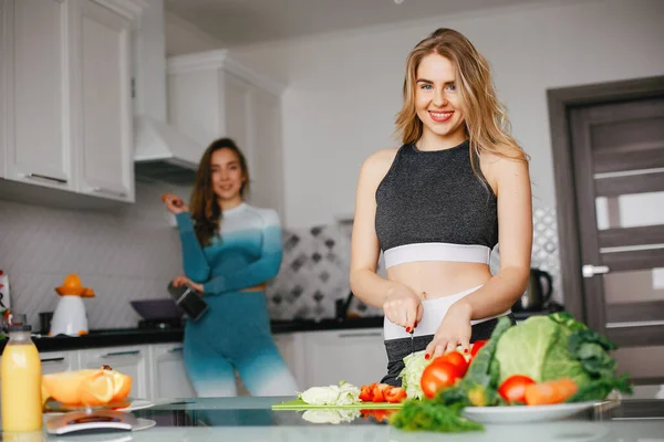 Två sporter flicka i ett kök med grönsaker — Stockfoto