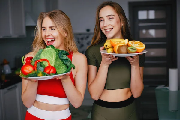 Twee sporten meisje in een keuken met groenten — Stockfoto