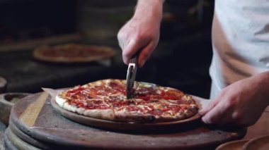Pizzayı yuvarlak bıçakla kesen erkek ellerinin yakın çekimi.
