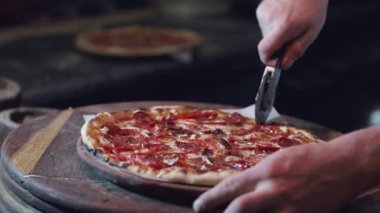 Pizzayı yuvarlak bıçakla kesen erkek ellerinin yakın çekimi.