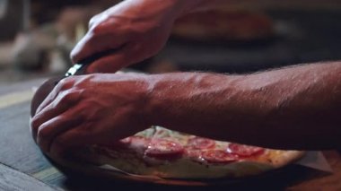 Pizzayı yuvarlak bıçakla kesen erkek ellerinin yakın çekimi.
