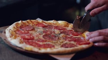 Pizzayı yuvarlak bıçakla kesen erkek ellerinin yakın çekimi.