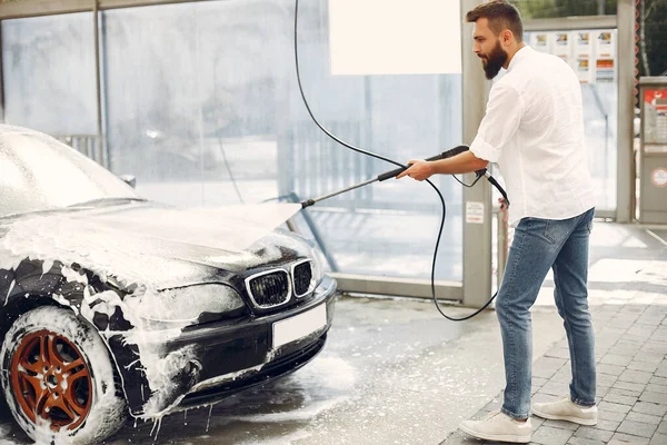 Hombre guapo en una camisa blanca lavando su coche — Foto de Stock