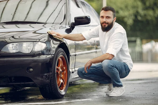 Un hombre con una camisa blanca limpia un auto en un lavado de autos —  Fotos de Stock