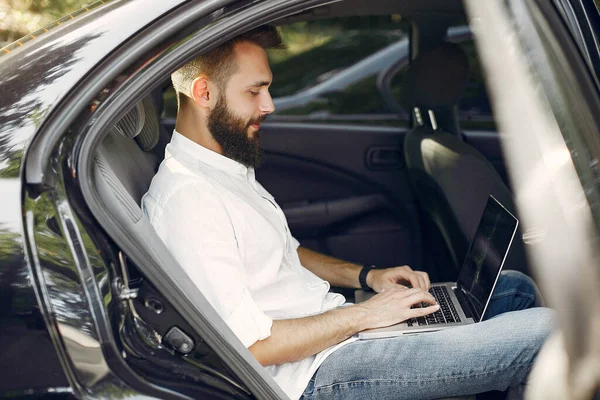 Стильный бизнесмен, сидящий в машине и пользующийся ноутбуком — стоковое фото