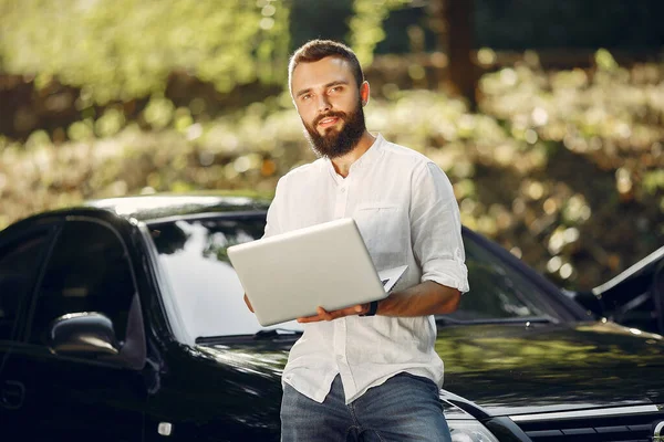 Стильный бизнесмен, стоящий рядом с машиной и пользующийся ноутбуком — стоковое фото