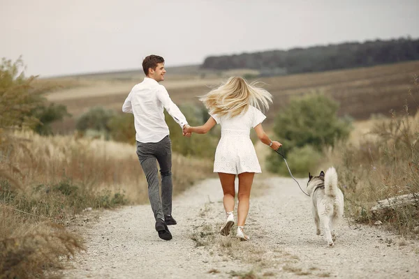 Casal em um campo de outono brincando com um cão — Fotografia de Stock