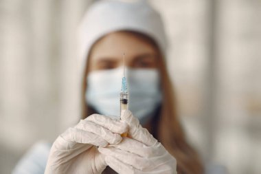 Elinde şırınga tutan maskeli ve üniformalı bir kadın.