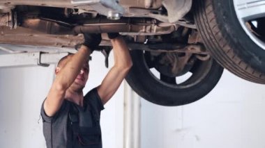 Servis merkezinde arabanın altında çalışan eldivenli tamirci.