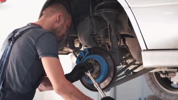 Mecánico en la rueda de reparación uniforme del coche en el centro de servicio — Vídeo de stock