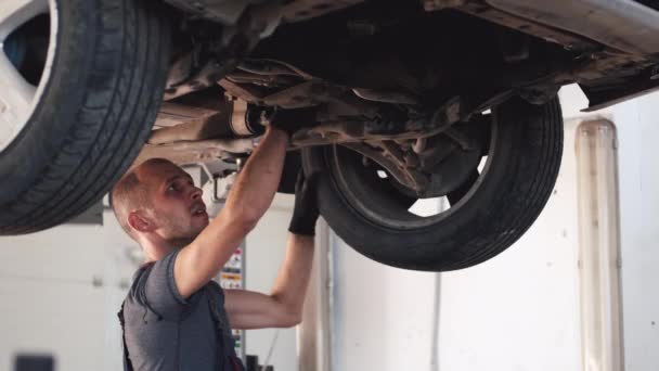 Mecánico en guantes trabajando bajo el coche en el centro de servicio — Vídeo de stock