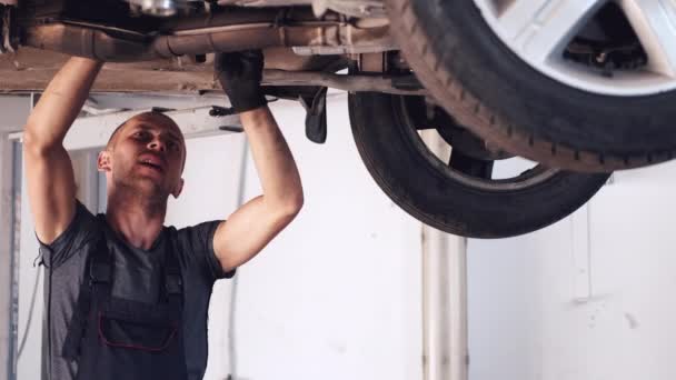 Mecánico en guantes trabajando bajo el coche en el centro de servicio — Vídeos de Stock