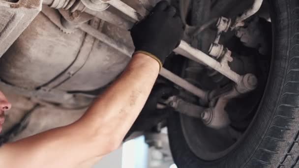 Mecánico en guantes trabajando bajo el coche en el centro de servicio — Vídeos de Stock