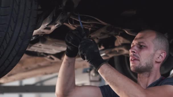 Mecánico en guantes trabajando bajo el coche en el centro de servicio — Vídeos de Stock