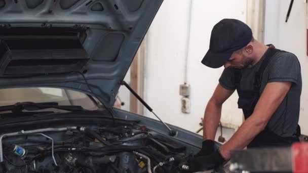 Mężczyzna w ciemnym mundurze naprawiający samochód klientów w garażu — Wideo stockowe