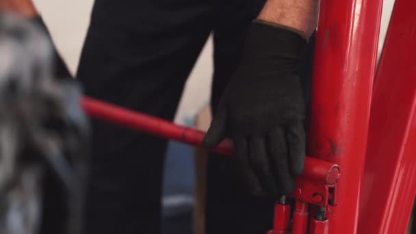 Pracownik fizyczny w rękawiczkach mocujących czerwoną konstrukcję w garażu — Wideo stockowe