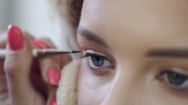 Makyaj sanatçısı salonda göz kalemiyle müşterilerin gözlerini çiziyor.