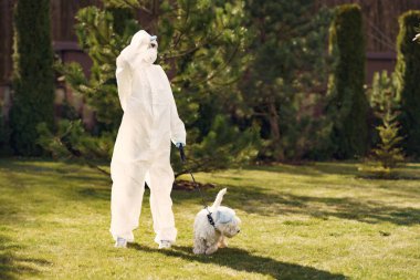Koruyucu kıyafetli bir kadın köpekle yürüyor.