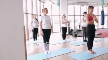 Modern bir spor salonunda bir eğitmenle esneme egzersizleri yapan kadınlar.