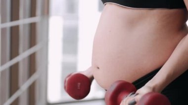 Spor kostümü giymiş hamile bir kadın egzersiz yapıyor.