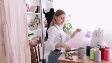 Kadın terzi, makas ve dikiş makinesiyle bir elbise üzerinde çalışıyor.