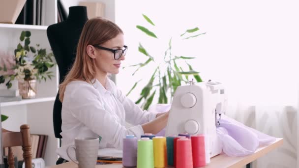 Glimlachende vrouw kleermaker is het naaien van een jurk met een naaimachine — Stockvideo